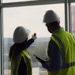 Two,construction,engineers,standing,indoors,near,big,window,looking,at